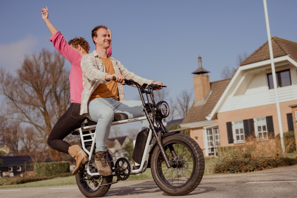 Een dynamische Astonic E-Ride in actie, met de bestuurder die vrij en wild door de stad zoeft, belichaamt de kernwaarden van duurzaamheid en innovatie tegen een stedelijke achtergrond, symboliserend de sociale impact en het streven naar een groenere toeko