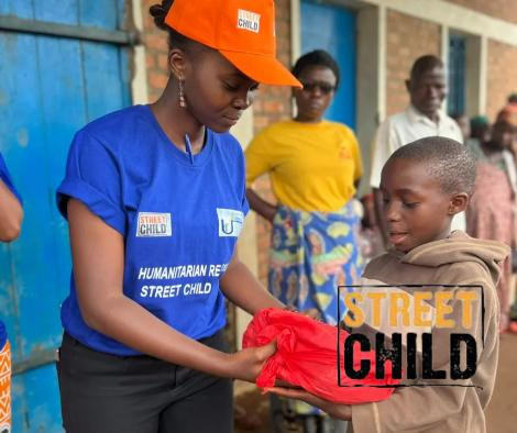 Een kind in Sierra Leone glimlacht terwijl het een boek ontvangt, omringd door dorpbewoners, symboliseert de impact van donaties aan Street Child door de samenwerking van Astonic.